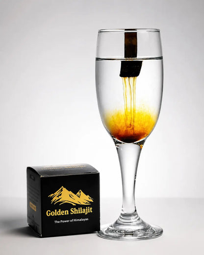 Glass of liquid with a black stick, next to a box labeled 'Golden Shilajit', on a white background
